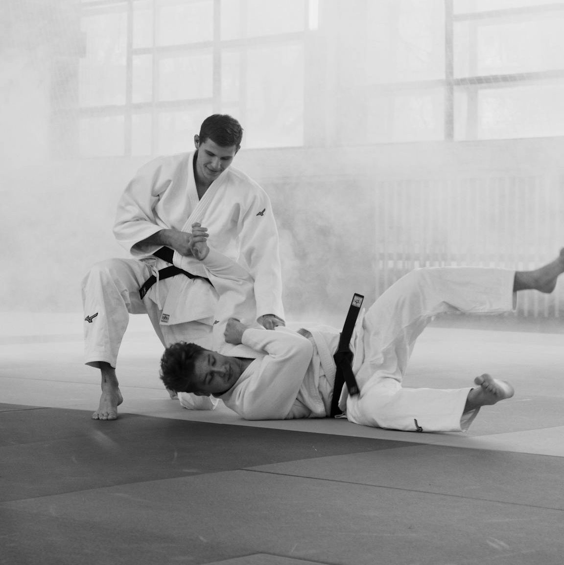 Two martial artists practicing judo in a misty indoor setting, displaying skill and intensity.